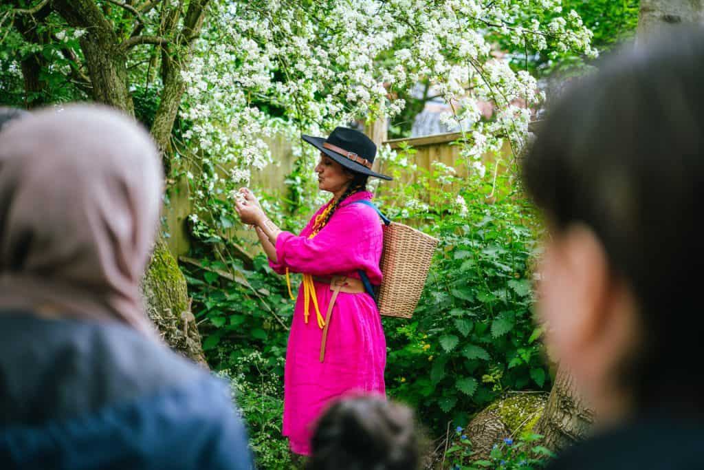 An asian woman in a pink dress picks some flowers from a tree